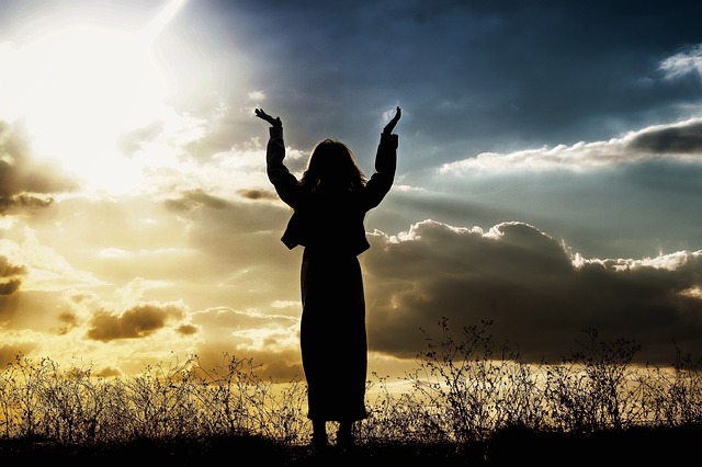 太陽に向かって手を挙げる女性のシルエット